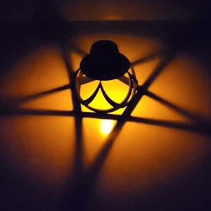 May include: A black metal lantern with a star-shaped design casts a warm glow on a dark surface.