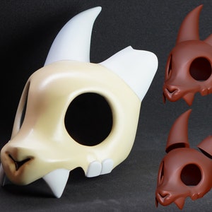 May include: A King mask from the animated series "The Owl House". The mask is primarily off-white with white horns and teeth, and a brown nose. Two additional brown masks are also shown.