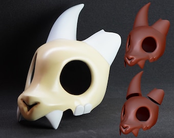 May include: A King mask from the animated series "The Owl House". The mask is primarily off-white with white horns and teeth, and a brown nose. Two additional brown masks are also shown.