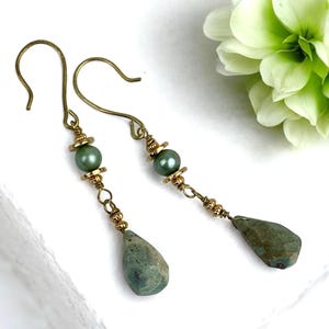 Peut inclure: Une paire de boucles d'oreilles pendantes en pierre verte avec des accents dorés. Les boucles d'oreilles présentent une petite perle verte et une pierre précieuse en forme de larme.