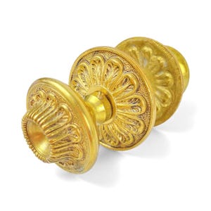 Peut inclure: Gros plan sur un bouton de porte doré avec un motif floral orné. Le bouton a une forme circulaire avec des motifs et des textures détaillés. La quincaillerie est probablement en métal et se détache sur un fond blanc.