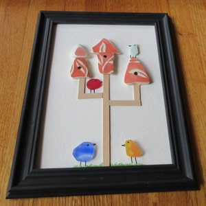 May include: A framed artwork featuring a tree with four birdhouses made of colorful glass. The tree is made of wooden sticks and the birdhouses are decorated with floral patterns. There are four birds made of glass, one red, one blue, one yellow, and one light blue.
