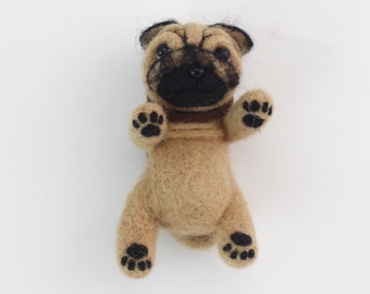 May include: A small, brown and black felt pug dog toy. The toy is lying on its back with its paws in the air.