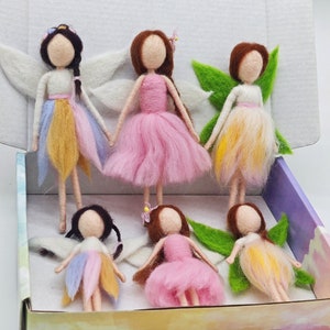 May include: Set of six felt fairy dolls with wings and colorful skirts. The fairies are arranged in a box with a purple and white background.
