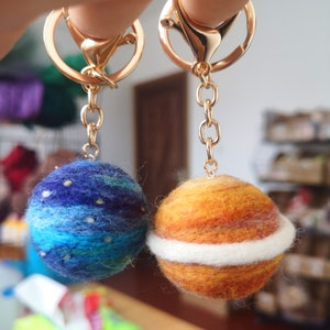May include: Two felt planet keychains, one blue with white stars and one orange with a white ring around the middle. Both are attached to gold key rings.