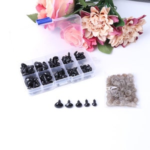 May include: A clear plastic storage box filled with black plastic safety eyes for crafts. The box has multiple compartments and is filled with different sizes of eyes. There is also a bag of loose safety eyes.
