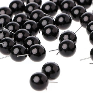 May include: A group of black plastic eyes with silver pins. The eyes are round and glossy.