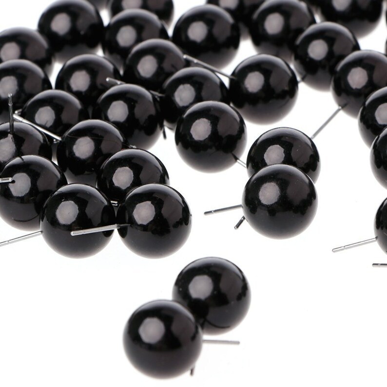 May include: A group of black plastic eyes with silver pins. The eyes are round and glossy.