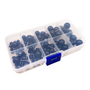 May include: A clear plastic storage box with a blue latch, filled with black plastic-headed push pins. The push pins are organized in rows in the box.