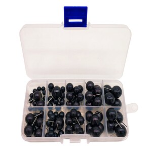 May include: A clear plastic storage box with a blue lid containing black push pins with round heads. The box has eight compartments, each filled with push pins.