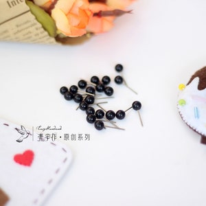 May include: A close-up of a collection of black push pins with silver metal heads. The pins are scattered on a white surface. The text "Easy Handmade,  童 手作り &middot; 原创 系列" is visible in the lower left corner of the image.