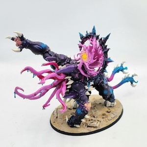 Puede incluir: Figura en miniatura detallada de una criatura monstruosa, pintada en tonos morados, azules y rosas. La figura presenta garras afiladas, tentáculos y una boca espinosa y abierta. Montada sobre una base ovalada texturizada.