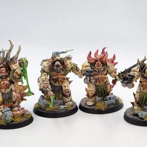 Può includere: Quattro figure in miniatura dettagliate e dipinte di Space Marines, ognuna con armi e armature uniche. Le figure sono in posa da combattimento, una tiene un'ascia grande e l'altra un bastone. Le figure sono dipinte in una varietà di colori, tra cui bianco, verde e marrone.