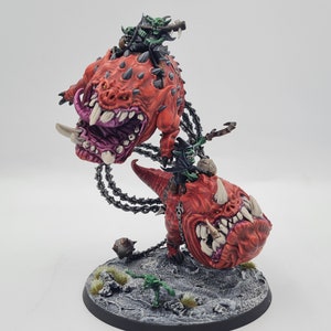 May include: A miniature wargaming figure set featuring two red, snarling, monstrous creatures with chains and three green goblin figures riding on top.
