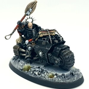 May include: A black and silver miniature of a Space Marine riding a motorcycle. The Space Marine is holding a staff with a skull at the top. The motorcycle has a skull on the side and a chain with a box on the back.
