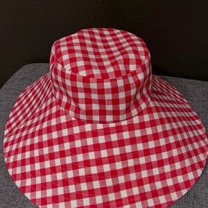K&ouml;nnte beinhalten: Ein Sonnenhut mit breiter Krempe und rot-wei&szlig;em Vichy-Muster. Der Hut hat eine runde Krone und eine breite, kreisf&ouml;rmige Krempe. Der Stoff ist in einem klassischen Karomuster gehalten.