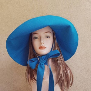 May include: A large, wide-brimmed sun hat in a vibrant blue color. The hat has a large bow tied at the front, also in blue.