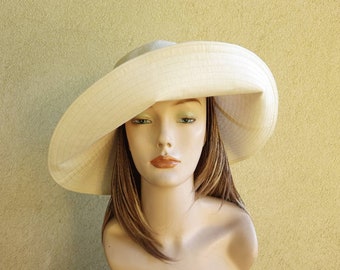 May include: A wide-brimmed, off-white sun hat with a slightly floppy brim. The hat is made of a woven fabric and has a simple, elegant design.