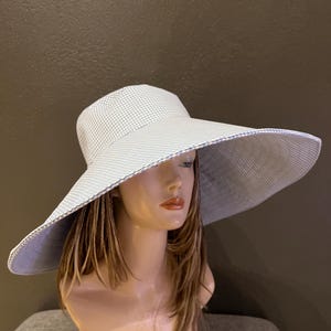 May include: A wide-brimmed sun hat with a light blue and white gingham pattern. The hat features a large brim and a matching interior lining. The hat is displayed on a mannequin head.