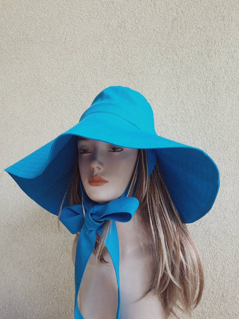 May include: A wide-brimmed sun hat in a bright turquoise blue. The hat has a large bow tied at the back.