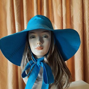 May include: A large, wide-brimmed sun hat in a bright turquoise blue. The hat has a wide brim and a simple design. The hat is tied with a bow at the neck.