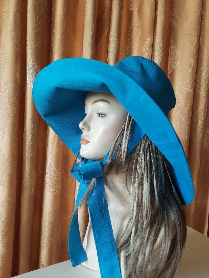 May include: A wide-brimmed sun hat in a vibrant turquoise blue. The hat has a large brim and a matching ribbon tied at the back of the neck.