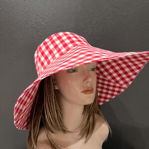 K&ouml;nnte beinhalten: Ein rot-wei&szlig; karierter Sonnenhut mit breiter Krempe. Der Hut wird auf einem Schaufensterkopf pr&auml;sentiert. Das Muster des Hutes ist ein klassisches Karomuster im Picknick-Stil.