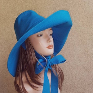 May include: A wide-brimmed sun hat in a bright blue color with a matching ribbon tied at the neck. The hat is made of a lightweight fabric and has a simple, elegant design.
