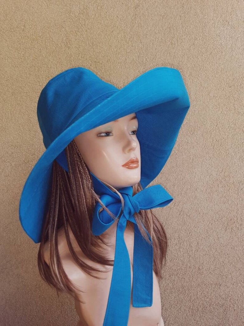 May include: A wide-brimmed sun hat in a bright blue color with a matching ribbon tied at the neck. The hat is made of a lightweight fabric and has a simple, elegant design.