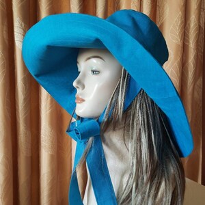 May include: A wide-brimmed sun hat in a vibrant turquoise blue. The hat has a large brim and a long, flowing tie that can be tied under the chin. The hat is made of a lightweight fabric and is perfect for protecting your face and neck from the sun.