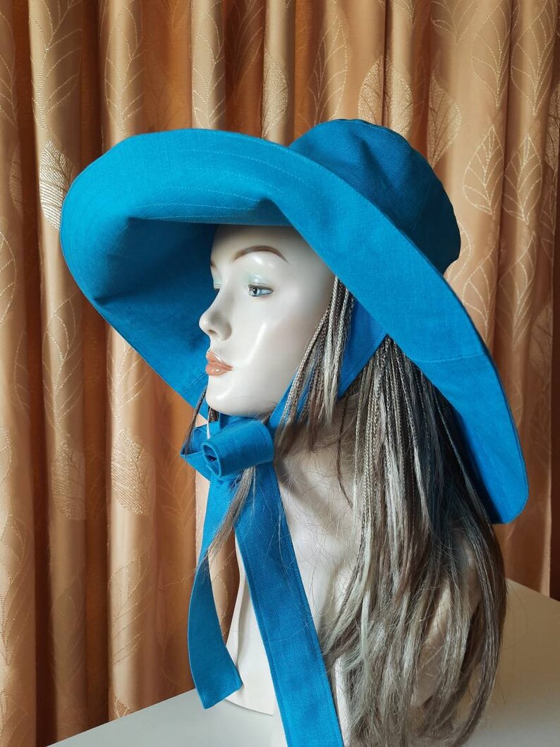 May include: A wide-brimmed sun hat in a vibrant turquoise blue. The hat has a large brim and a long, flowing tie that can be tied under the chin. The hat is made of a lightweight fabric and is perfect for protecting your face and neck from the sun.