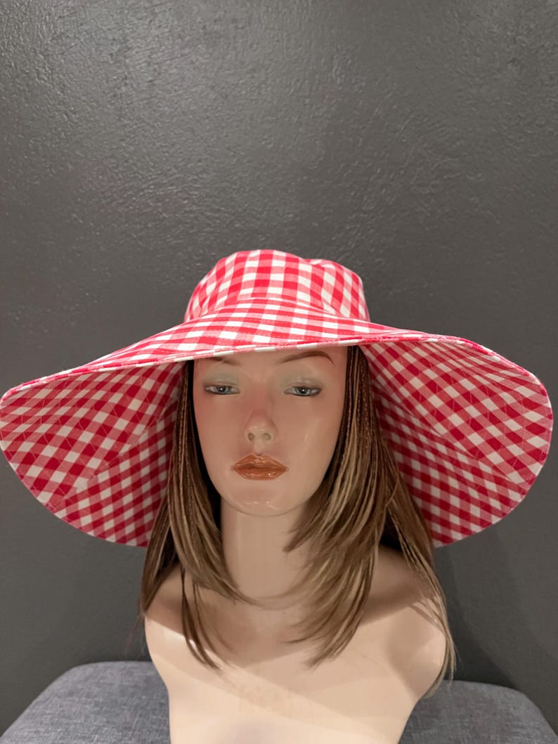 K&ouml;nnte beinhalten: Ein Sonnenhut mit breiter Krempe und einem rot-wei&szlig; karierten Vichy-Muster. Der Hut hat eine gro&szlig;e Krempe und ein klassisches, sommerliches Design. Ein stilvolles Accessoire f&uuml;r Outdoor-Aktivit&auml;ten.