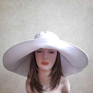 May include: A large, white sun hat with a wide brim. The hat is made of a soft, lightweight fabric and has a simple, elegant design.
