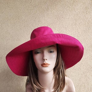 May include: A bright fuchsia sun hat with a wide brim. The hat is made of a textured fabric and has a classic design. The hat is displayed on a mannequin head with long, layered hair.