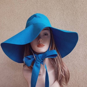 May include: A wide-brimmed sun hat in a bright blue color. The hat has a large brim and a matching blue ribbon tied at the neck.