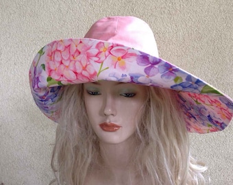 Pode incluir: Um chapéu de sol rosa com aba larga e estampa floral com hortênsias rosa, roxas e brancas.