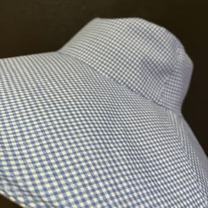 May include: A blue and white gingham sun hat with a wide brim. The hat is made of a soft fabric and has a classic, timeless design. The hat is perfect for protecting the face and neck from the sun.