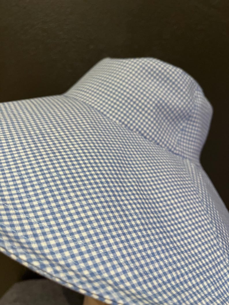 May include: A blue and white gingham sun hat with a wide brim. The hat is made of a soft fabric and has a classic, timeless design. The hat is perfect for protecting the face and neck from the sun.