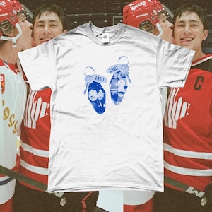 May include: White t-shirt with two blue key-shaped designs, each bearing numbers: "1410" and "1221". The shirt is displayed against a backdrop of hockey players in red jerseys and helmets.