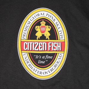 May include: A yellow and red circular label with the text "PREMIUM GLOBAL PONK SKA TYPE" and "CITIZEN FISH" in a black font. The label also includes a small image of a crown and two figures in red, white, and yellow. The text "It's a fine line" is printed in black below the label.