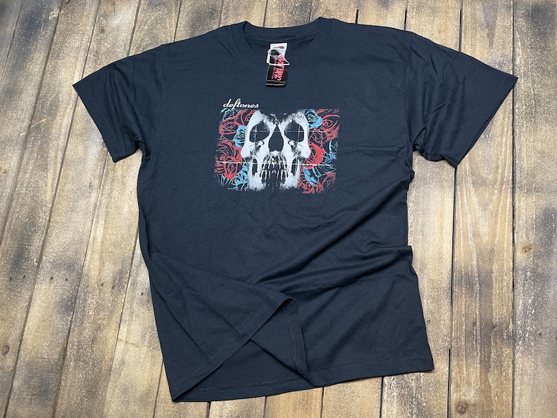 May include: Black t-shirt with a white skull graphic and red and blue roses. The text "Deftones" is printed on the shirt.