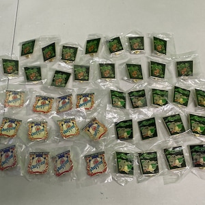 May include: A collection of 50 enamel pins in individual plastic bags. The pins feature various designs, including green and red cartoon characters, and a blue and gold shield with the text "Back for the Attack".