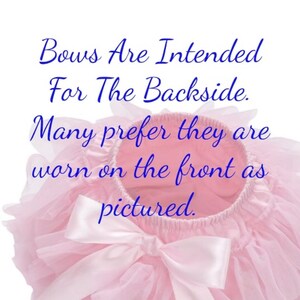 May include: A pink tulle tutu with a large white satin bow. The text "Bows Are Intended For The Backside. Many prefer they are worn on the front as pictured." is written in blue text on the tutu.