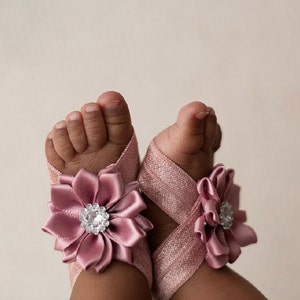 May include: A pair of pink baby sandals with a satin flower embellishment and a rhinestone center.
