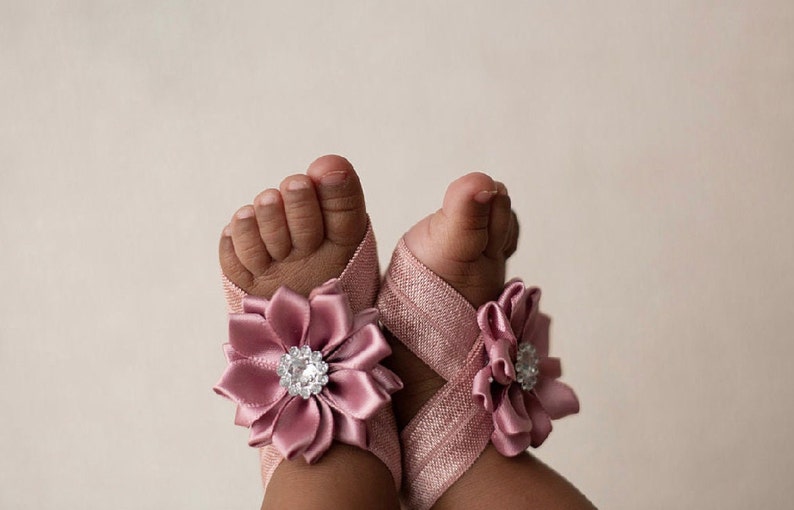 May include: A pair of pink baby sandals with a satin flower embellishment and a rhinestone center.