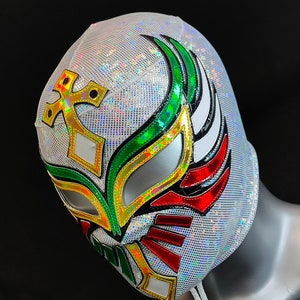 Op de afbeelding: Een wit worstelmasker met groene, rode en gouden accenten. Het masker heeft een kruisontwerp aan de bovenkant en een vleugelontwerp aan de zijkant.