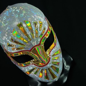 Op de afbeelding: Een wit worstelmasker met gouden en rode accenten. Het masker heeft een groot, iriserend ontwerp aan de voorkant.