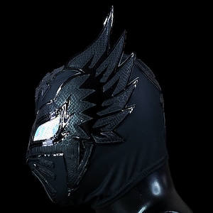Op de afbeelding: Zwart worstelmasker met een groot, zwart, schubbig vleugelontwerp aan de zijkant. Het masker heeft een zilveren, reflecterende oogopening.
