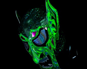 May include: Green and black wrestling mask with a detailed design featuring a monster face with sharp teeth and horns. The mask has a mesh eye covering and a shiny finish.