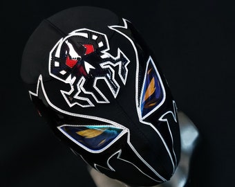 Pode incluir: Máscara de luta livre preta com um design de aranha branca e orifícios para os olhos azuis e laranja.